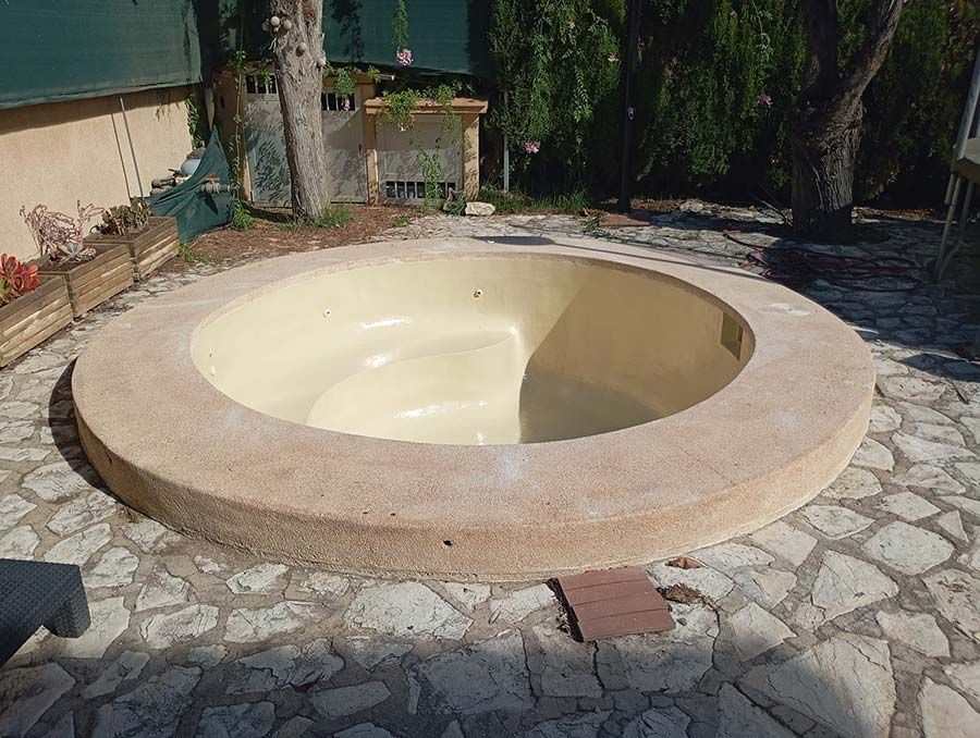 Piscina circular vacía y enterrada rodeada de un patio de hormigón y piedra en un patio.