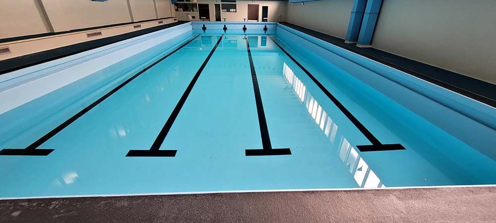 Una piscina cubierta con líneas negras en los carriles y agua azul clara que refleja la luz natural.