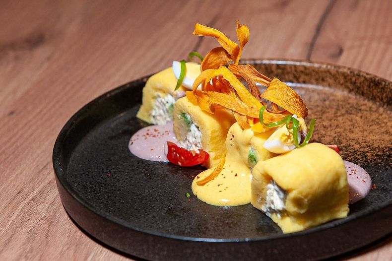 Postre emplatado con pastelitos enrollados, crema, fresas y un toque de naranja en un plato oscuro