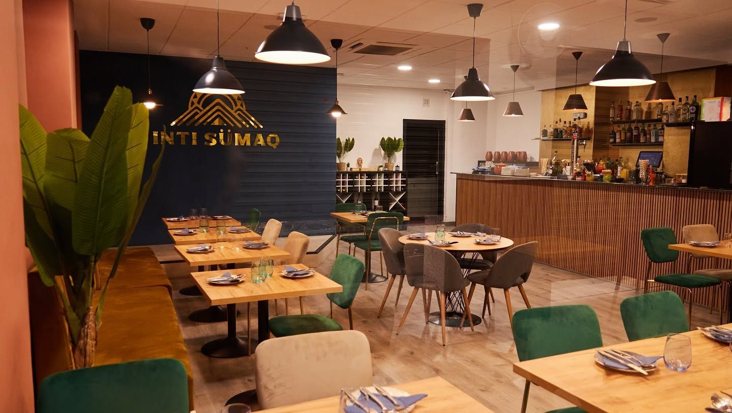 Acogedor interior de restaurante con mesas de madera, sillas verdes, luces colgantes y una barra a rayas.