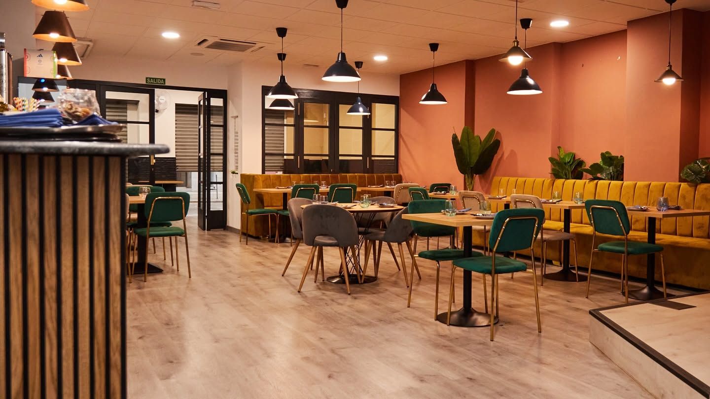 Cafetería moderna vacía con mesas de madera, sillas verdes, cálidas lámparas colgantes y paredes naranjas