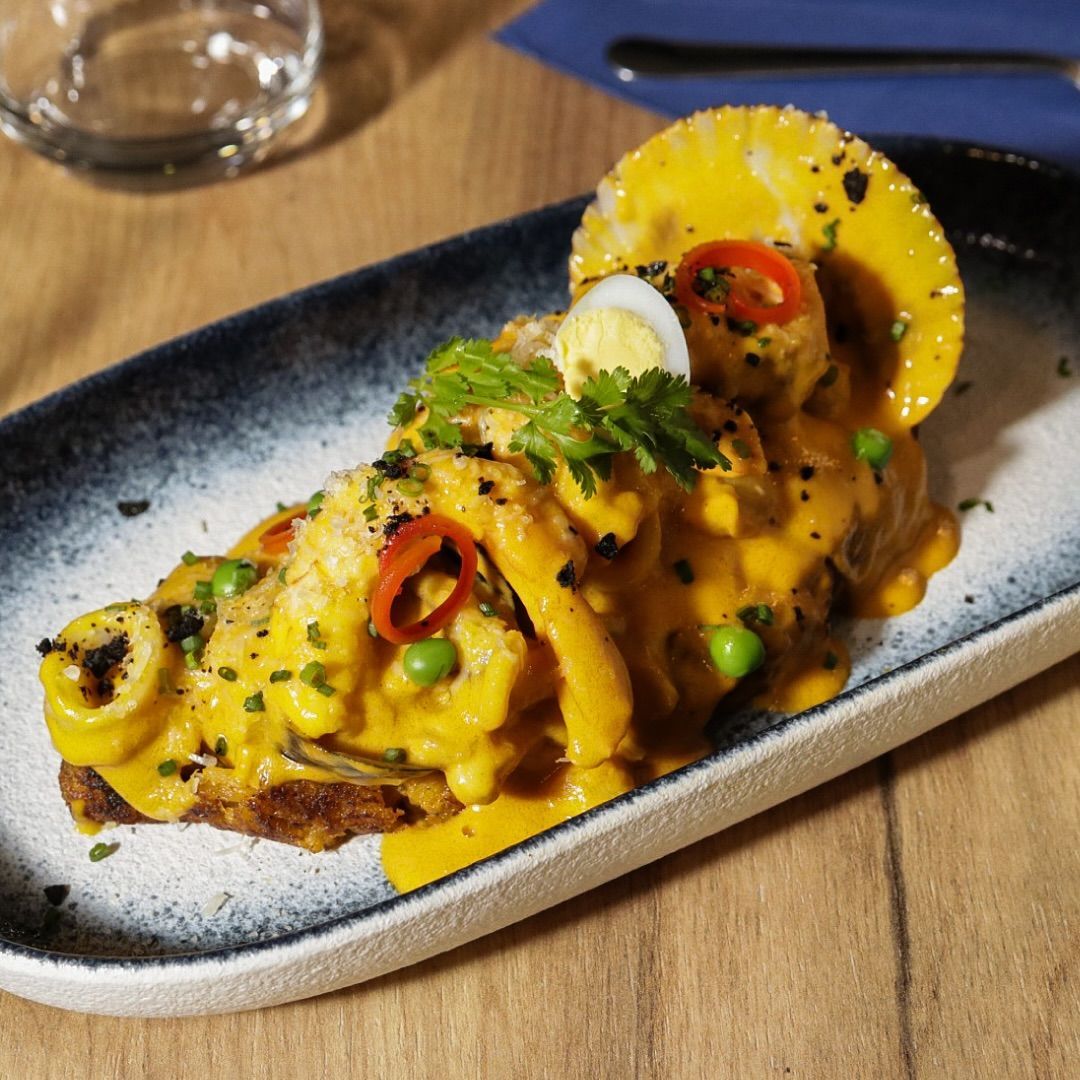 Plato de pescado emplatado con salsa amarilla, guisantes, chiles rojos y una rodaja de limón en un plato rectangular negro
