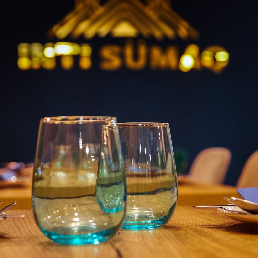 Dos vasos azulados sobre una mesa de restaurante, con luces cálidas desenfocadas al fondo