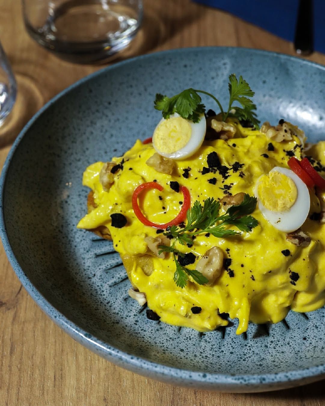 Pasta amarilla con huevo cocido en rodajas, hierbas y chile rojo en un plato azul