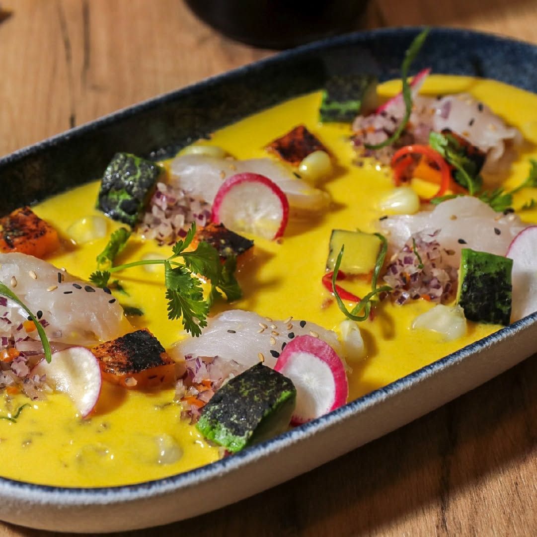 Curry amarillo servido con rábano en rodajas, hierbas y pescado sellado en un plato negro