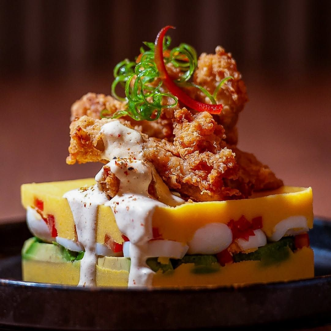 Pollo frito crujiente sobre una base de polenta amarilla en capas, con salsa cremosa y guarnición verde