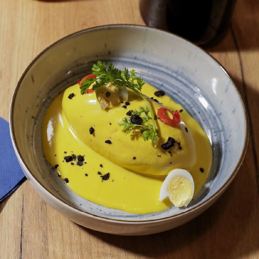 Plato cremoso de color amarillo brillante en un cuenco de cerámica, adornado con hierbas, chile y migas sobre una mesa de madera