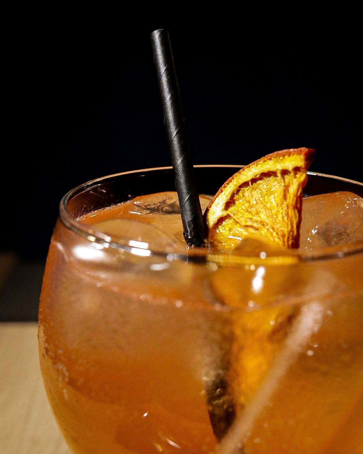 Cóctel naranja con una pajita negra y una rodaja de naranja deshidratada en una copa