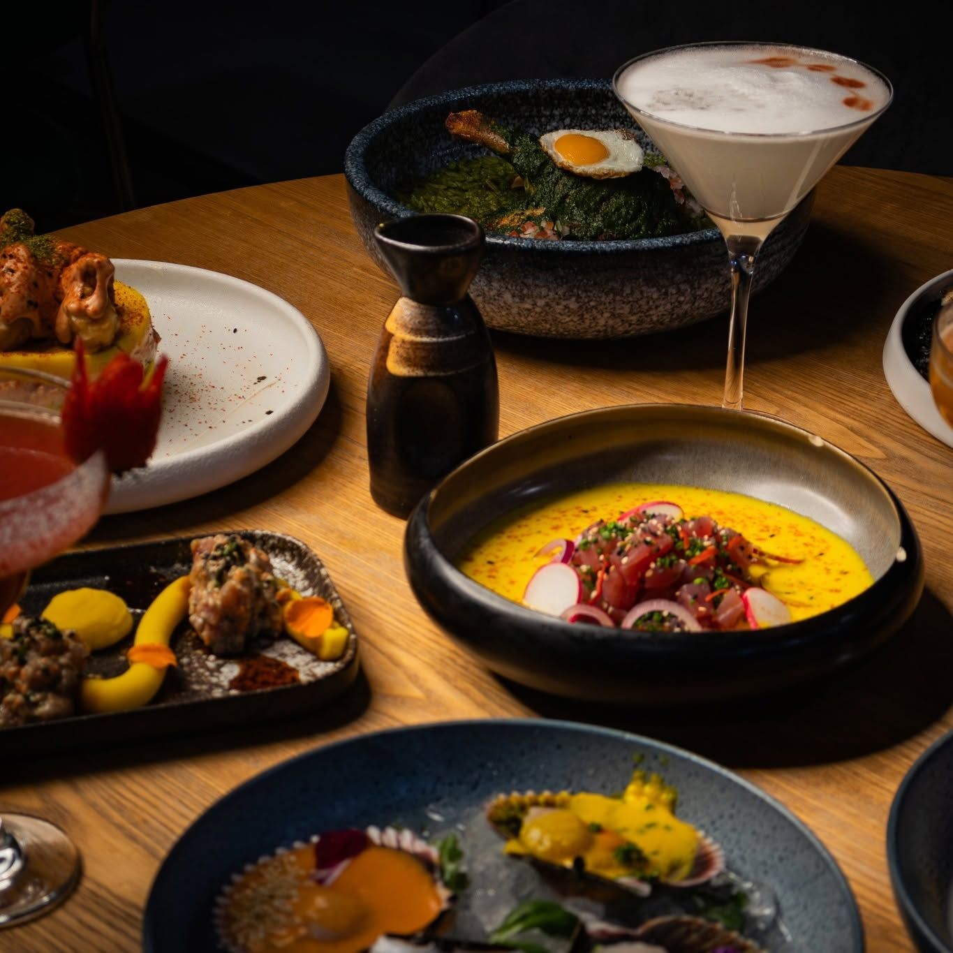 Una selección de platos gourmet y cócteles sobre una mesa de comedor con luz tenue