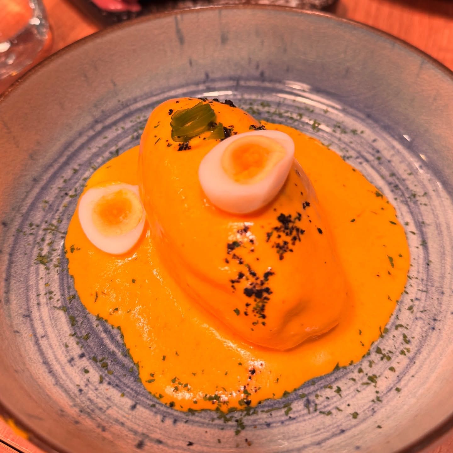 Postre de naranja en un plato de cerámica, cubierto con trozos de merengue blanco y guarnición verde.