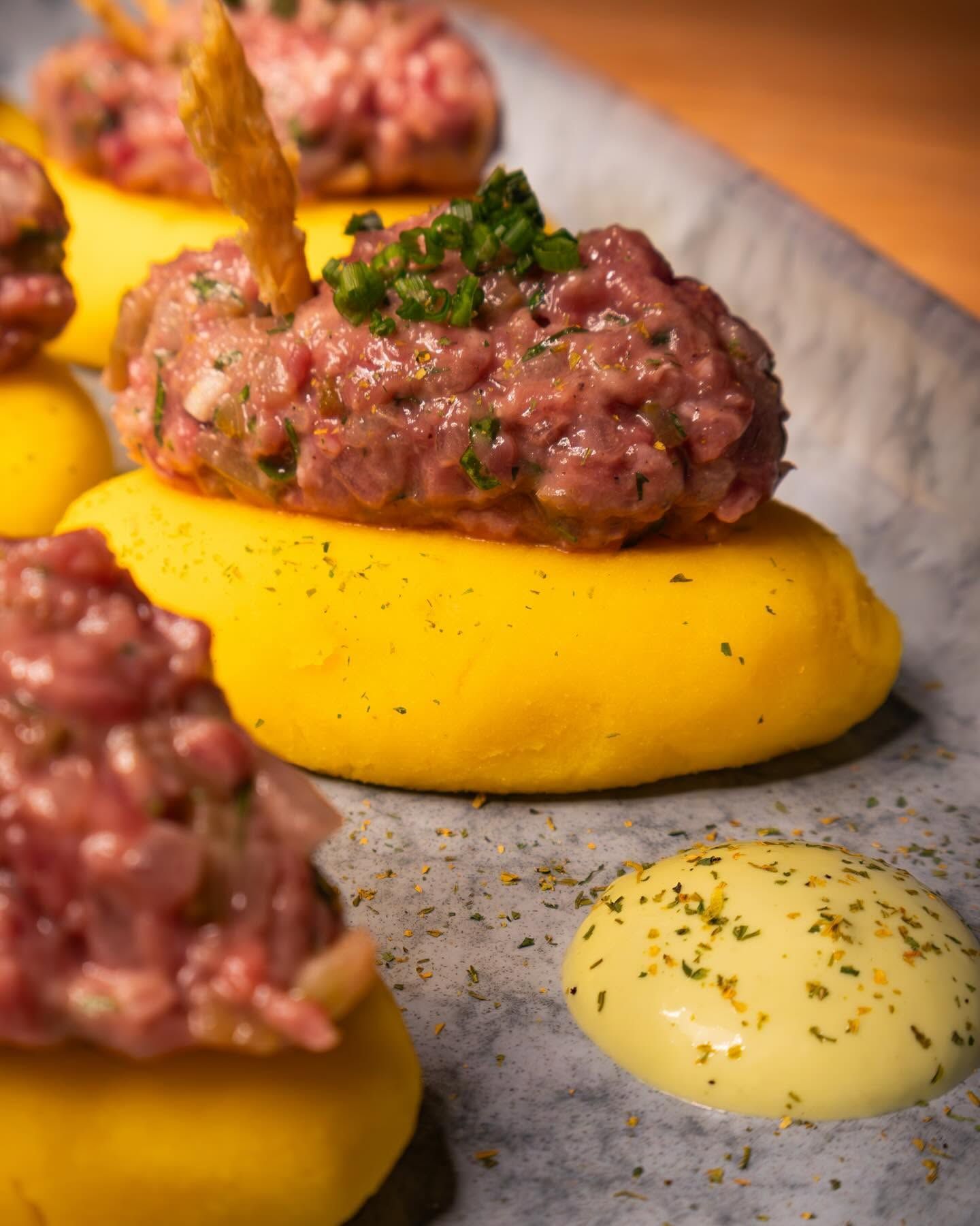 Primer plano de tartar de ternera crudo sobre puré amarillo intenso, con hierbas y salsa cremosa, servido en un plato