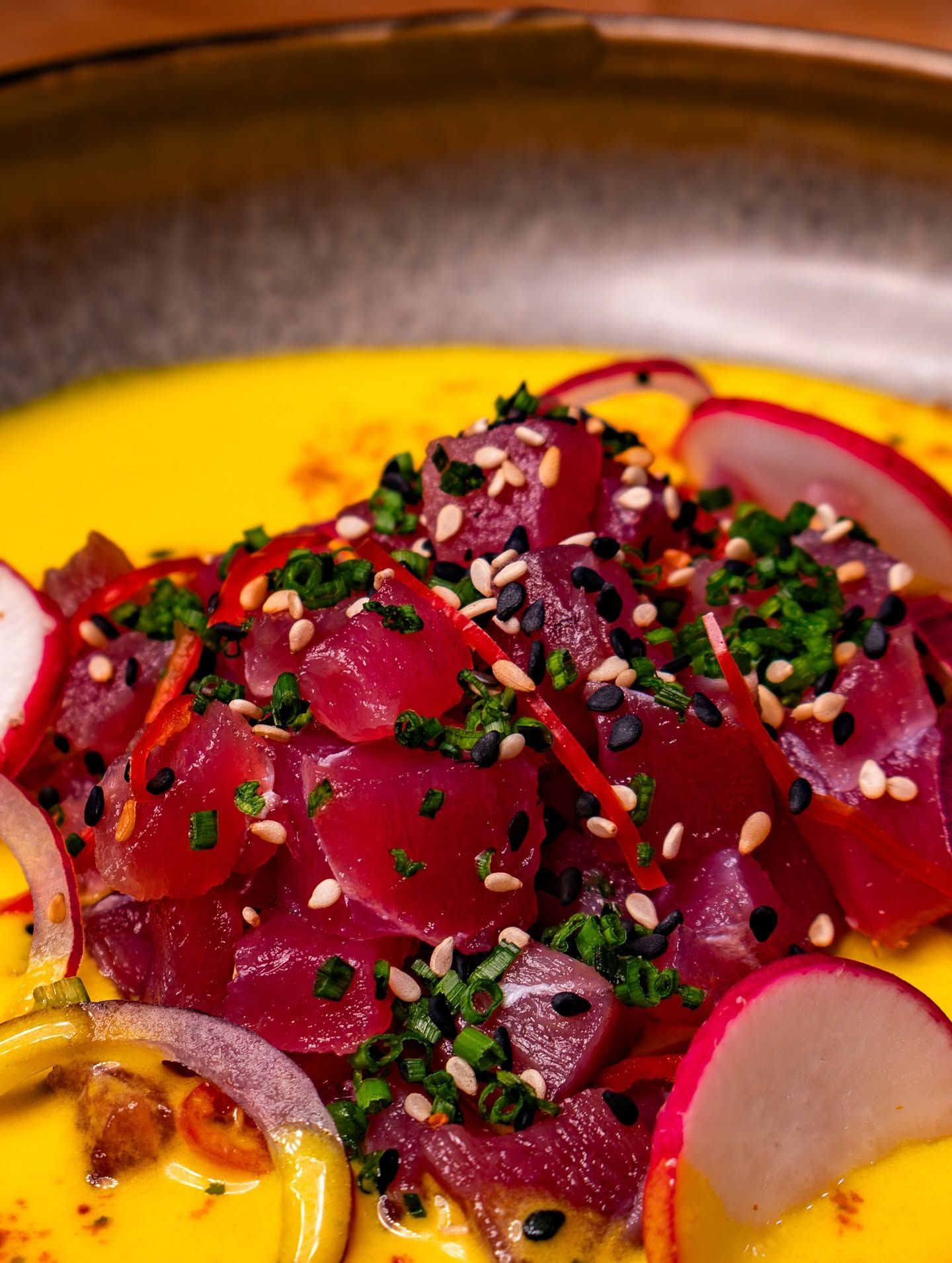 Tartar de atún en láminas con semillas de sésamo, cebollino y rábano sobre una salsa de color amarillo intenso