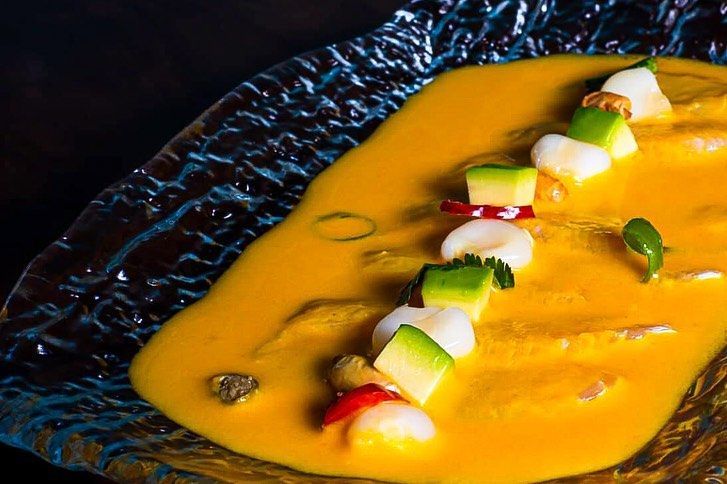 Plato gourmet emplatado con salsa de naranja y una línea de verduras cortadas en dados sobre un plato oscuro