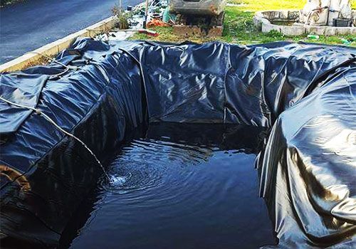 Bassin ou réservoir d'eau extérieur recouvert de plastique noir, l'eau reflétant la lumière du soleil