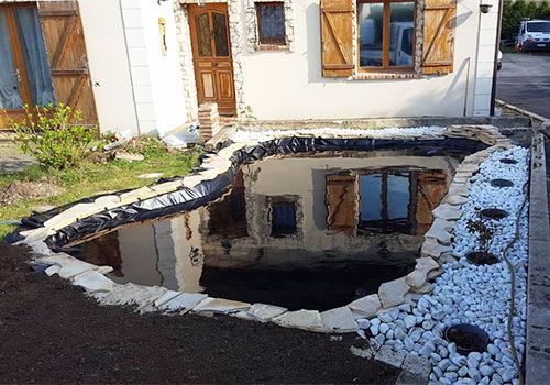 Terrasse arrière avec un bassin sombre et réfléchissant, bordé de rochers blancs, à côté d'une maison.