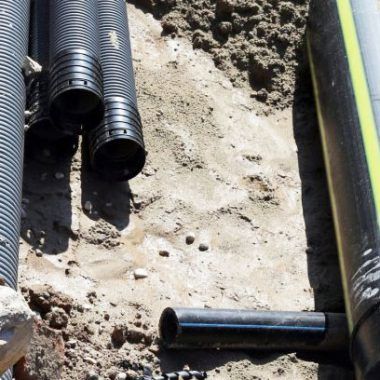 Des tuyaux ondulés noirs et un câble jaune sur du gravier sur un chantier de construction