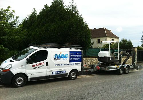 Une camionnette de service blanche tractant une remorque chargée de matériel est stationnée en bord de route, près de maisons et d'arbres.