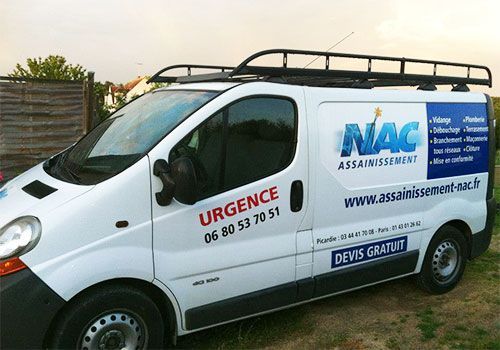 Fourgonnette blanche de service NAC Assainissement avec galerie de toit et coordonnées de contact urgentes, stationnée à l'extérieur