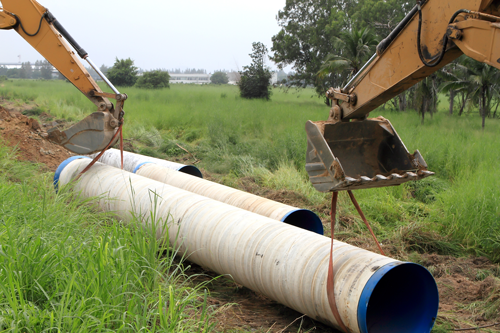 Deux excavatrices soulèvent un grand pipeline blanc dans un champ herbeux