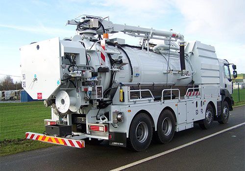 Camion aspirateur industriel blanc stationné sur une route à côté d'un champ herbeux