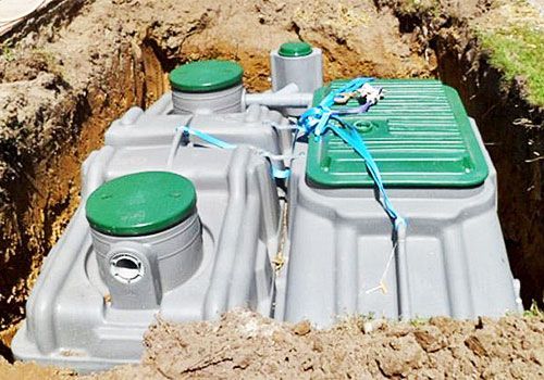 Réservoirs en plastique avec couvercles verts installés dans un trou creusé dans le sol