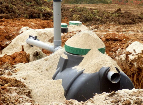 Installation d'une fosse septique avec tuyaux gris et cuve souterraine recouverte de sable sur un chantier de construction
