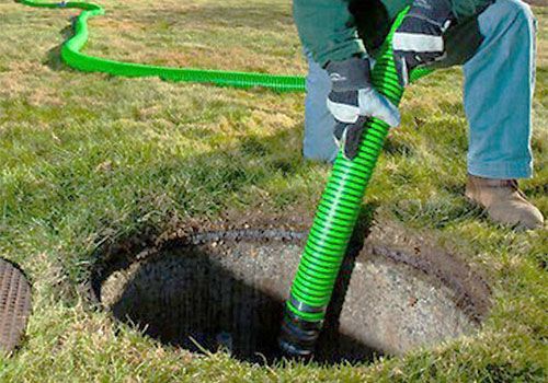Un ouvrier utilise un tuyau d'aspirateur vert pour dégager les débris d'un trou souterrain rond dans une cour herbeuse.