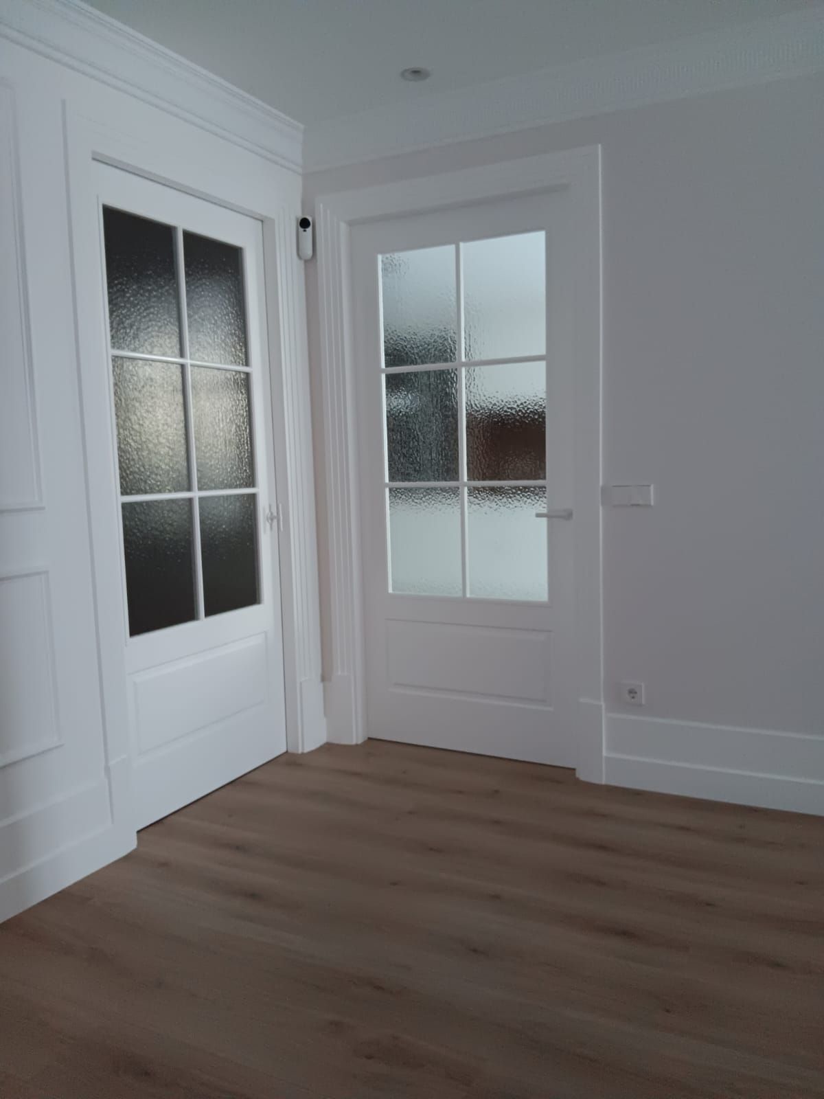 Habitación blanca vacía con puertas de vidrio esmerilado y suelo de madera clara.