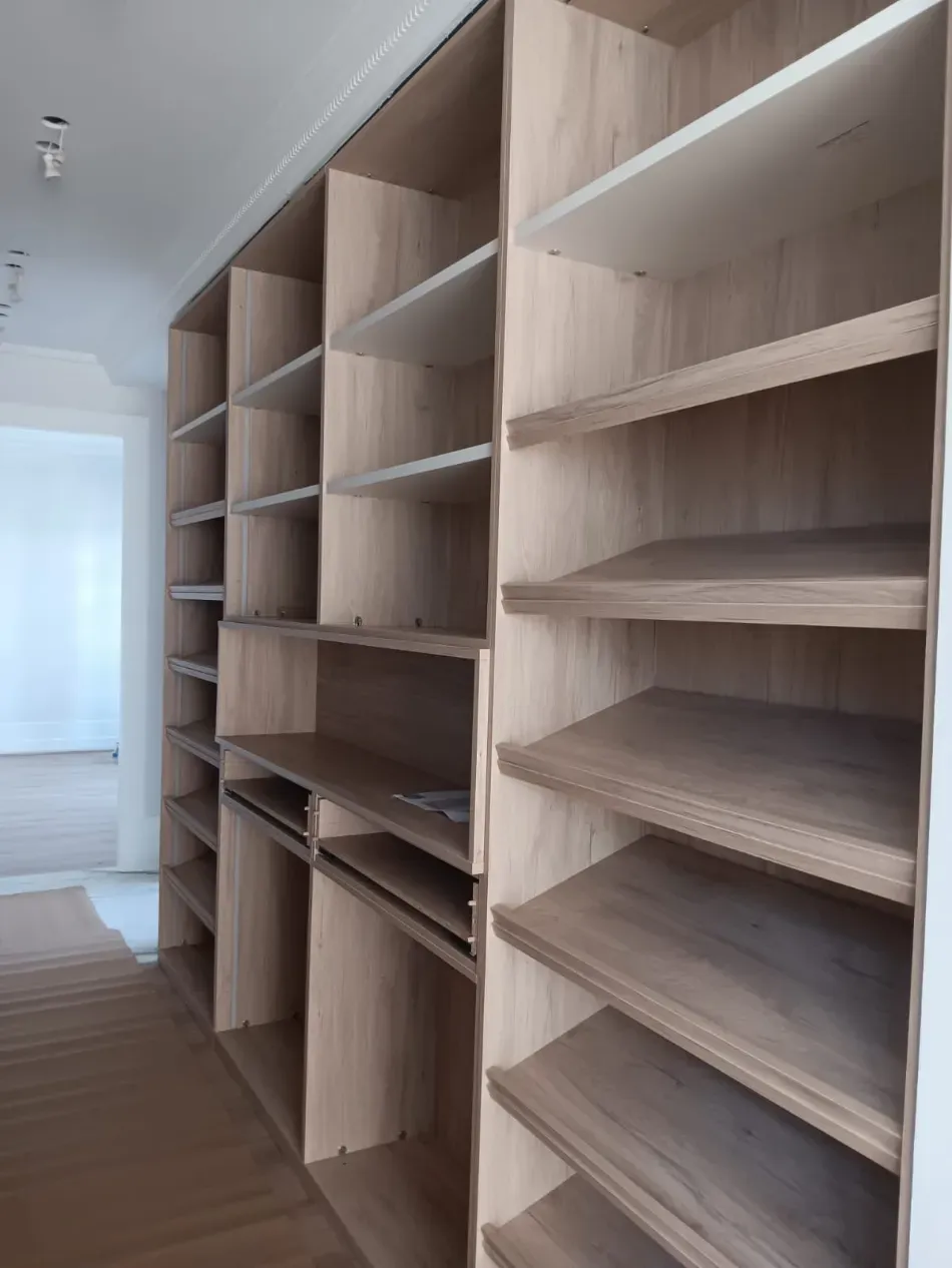 Estantería con paneles de madera y filas de gorras de béisbol, junto a una pared de luces blancas redondas.