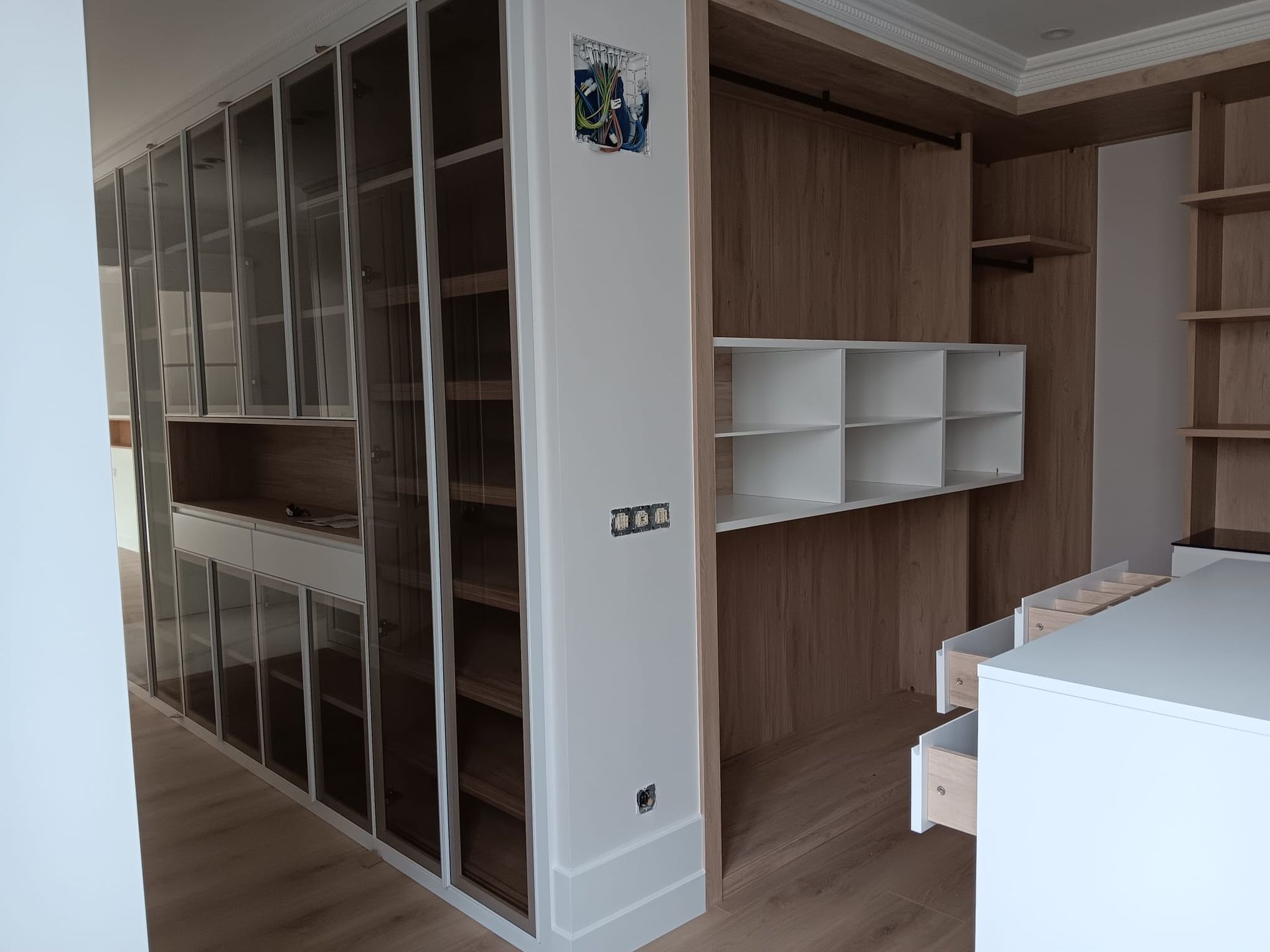 Armarios y estantes de madera empotrados en una habitación moderna con estantes y encimeras blancas.