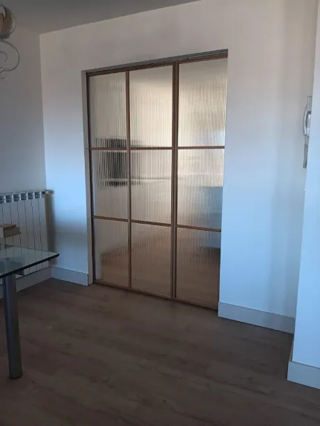 Pasillo luminoso con suelo de madera, puerta arqueada y un dormitorio visible a través de una puerta abierta.