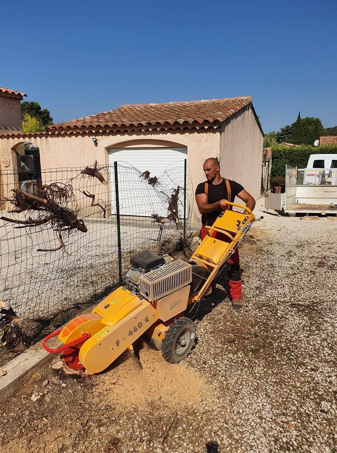 Intervention d'un élagueur devant l'entrée d'une maison individuelle pour un débroussaillage près d'un grillage