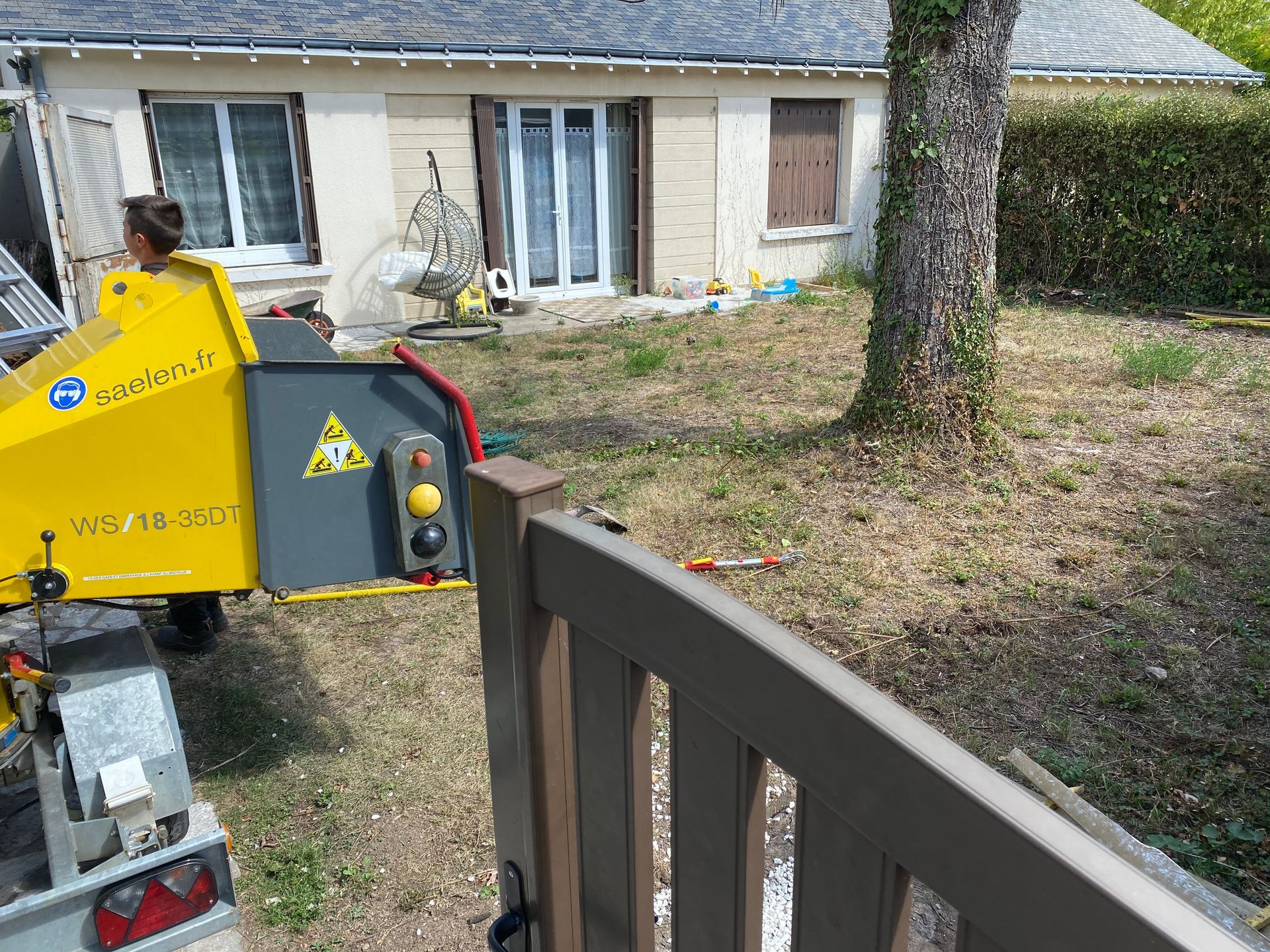 Début d'un chantier de terrassement paysager en jardin individuel avec un arbre au milieu et le matériel d'élagage à gauche