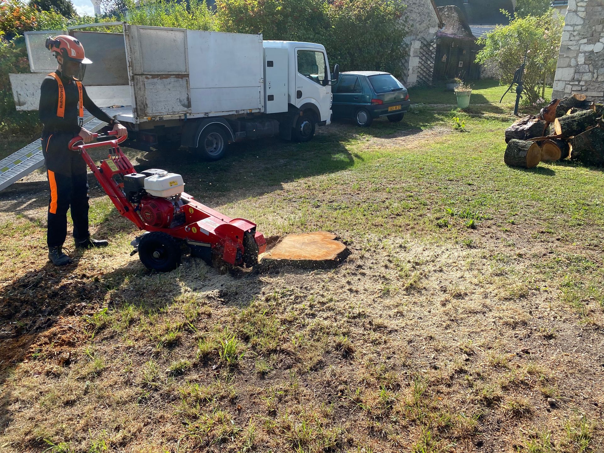 Intervention d'un élagueur en combinaison et avec casque pour le rognage d'une souche dans un jardin
