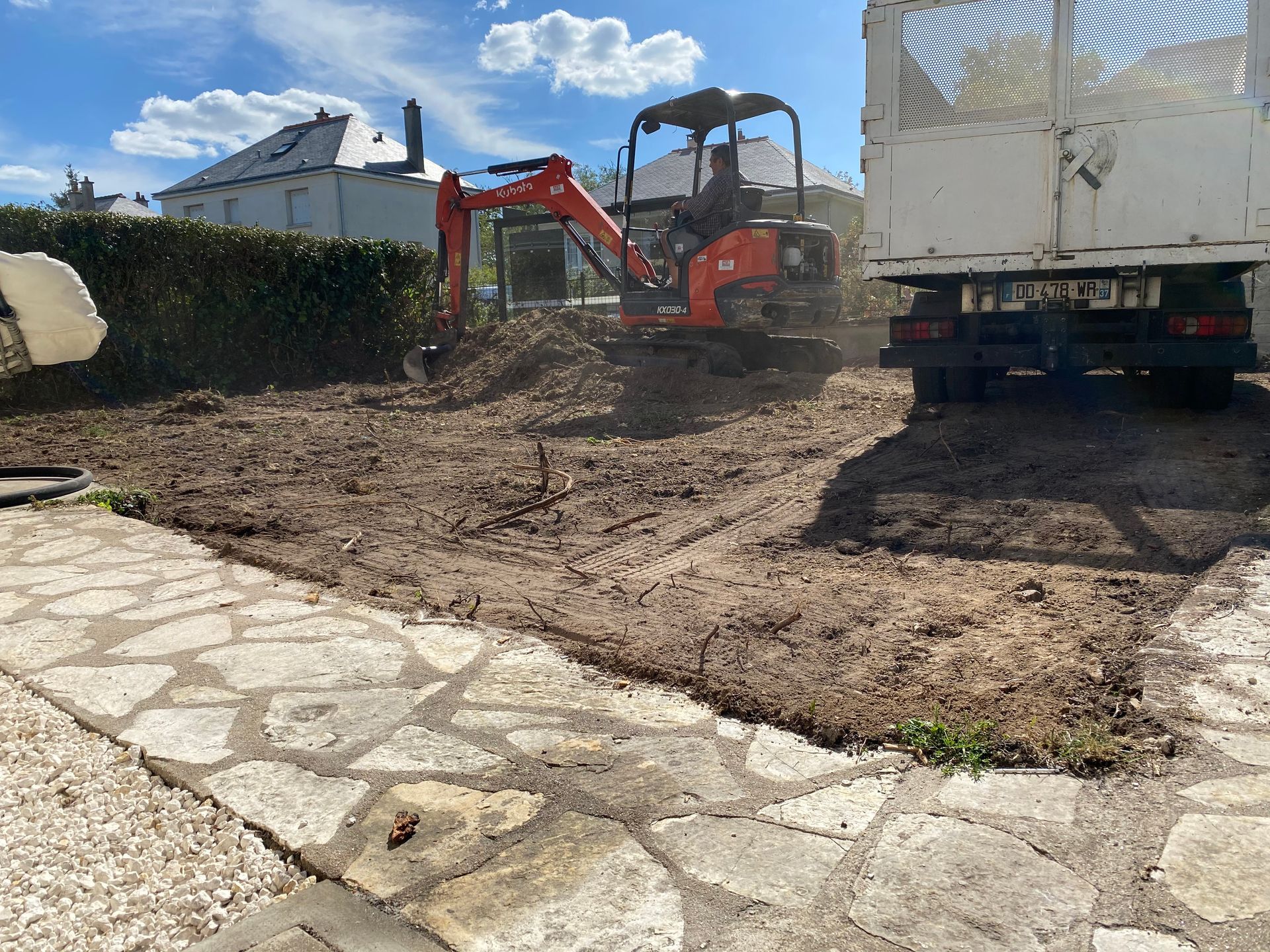 Début du terrassement paysager d'un jardin avec suppression de la pelouse, le camion à droite et une pelleteuse au centre