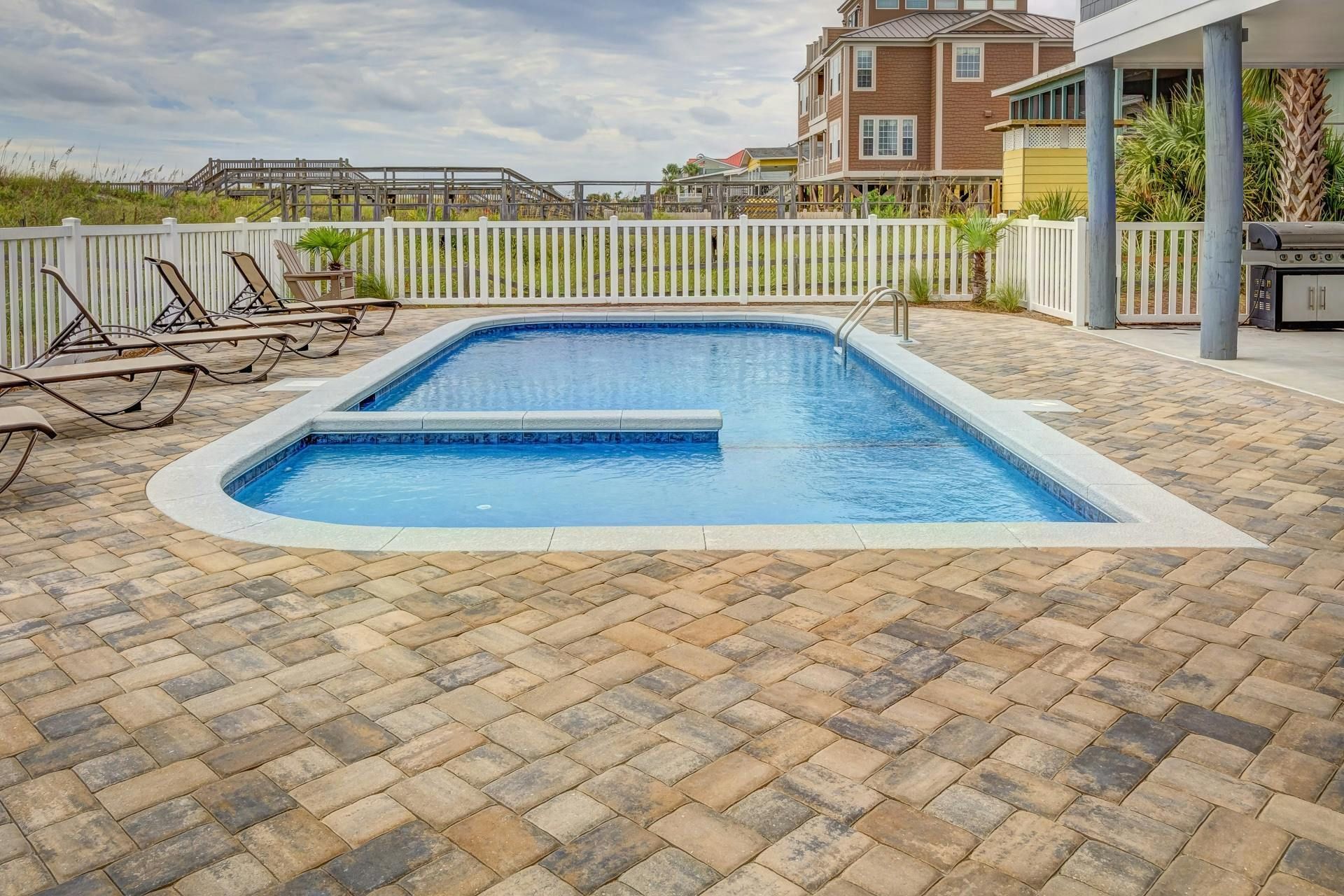 Una gran piscina está rodeada por un patio de ladrillo y sillas.