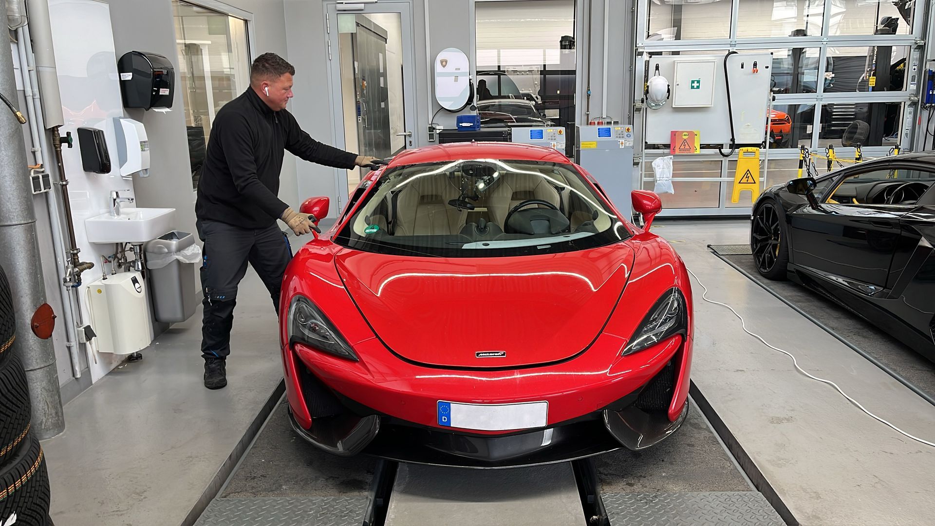 Ein Mann arbeitet in einer Garage an einem roten Sportwagen.
