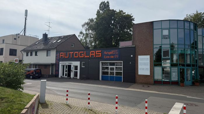 Autoglas-Werkstatt mit orangefarbenem Schild, Glasfassade und geparkten Autos an einer Straßenecke