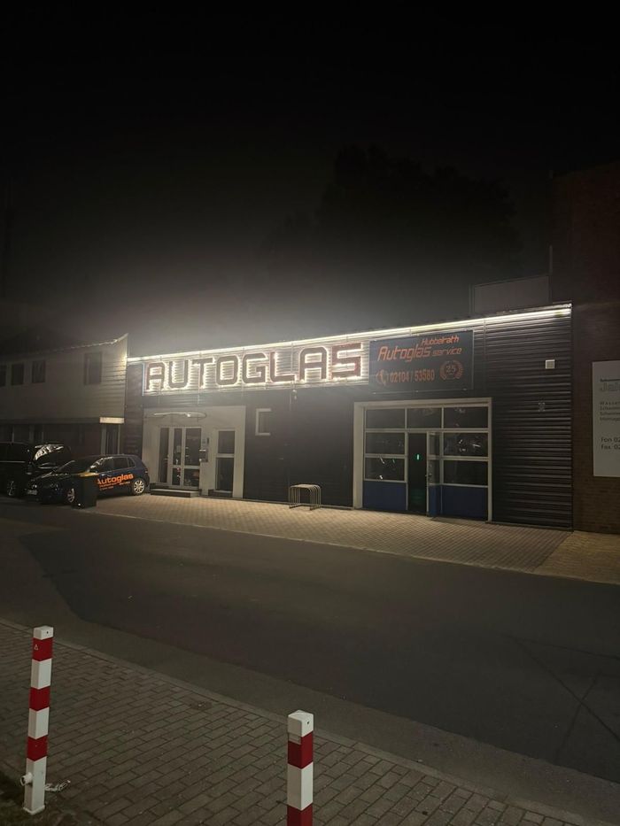 Nächtliche Straßenansicht eines beleuchteten Ladengeschäfts in Douglas mit davor geparkten Autos.