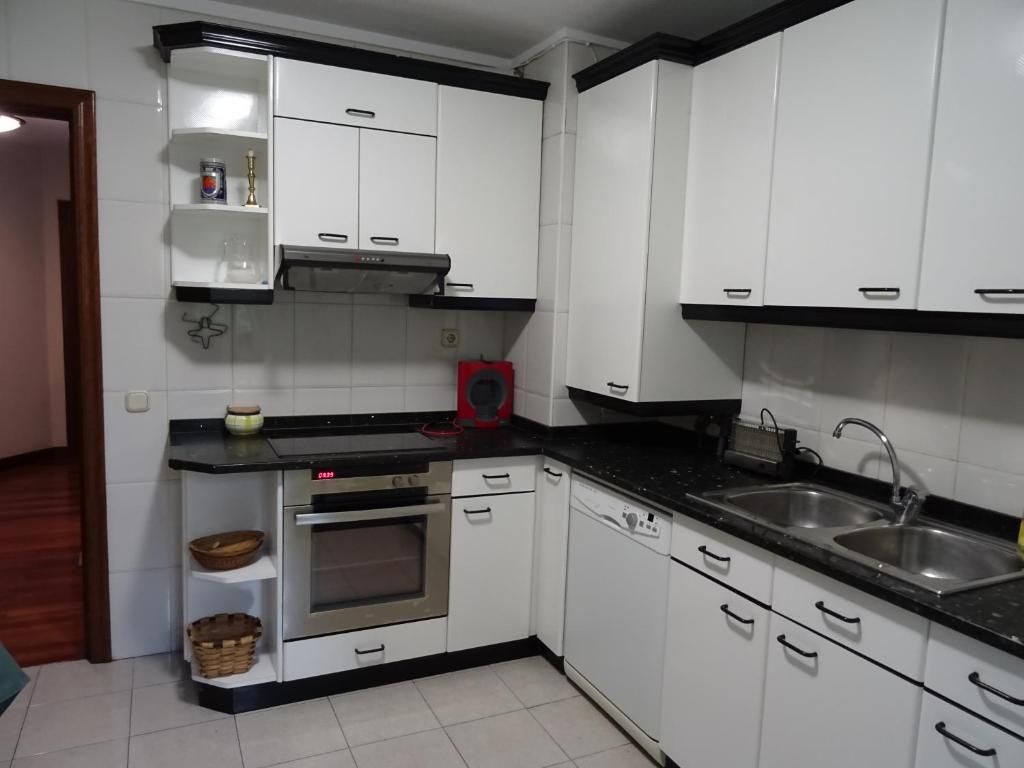 Gabinetes de cocina blancos con detalles negros, encimeras negras y electrodomésticos de acero inoxidable.