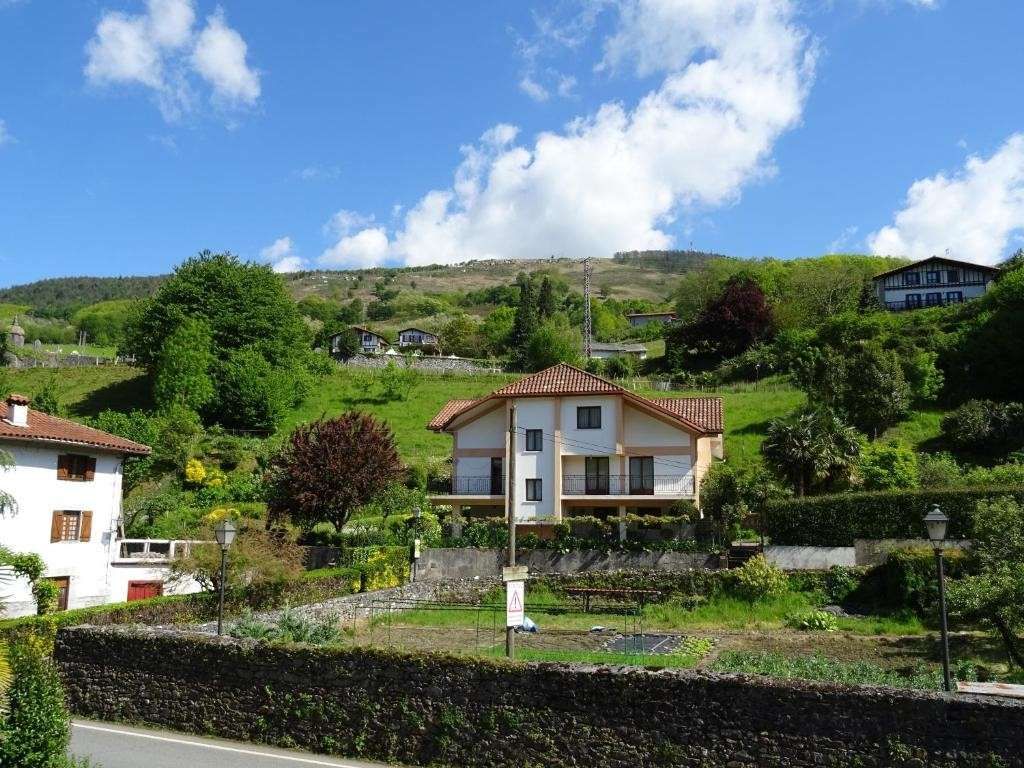 Casas en una ladera verde bajo un cielo azul con nubes esponjosas.