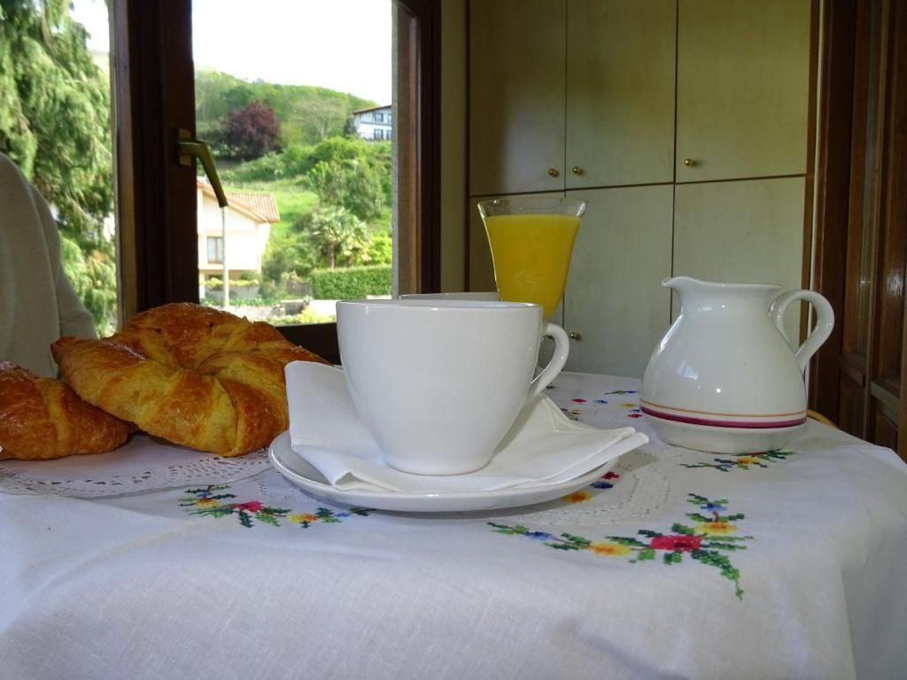 Mesa de desayuno con café, croissants, jugo y crema, cerca de una ventana con vista.