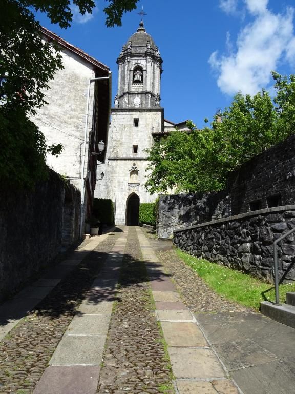 Camino de piedra que conduce a una iglesia con campanario bajo un cielo azul.