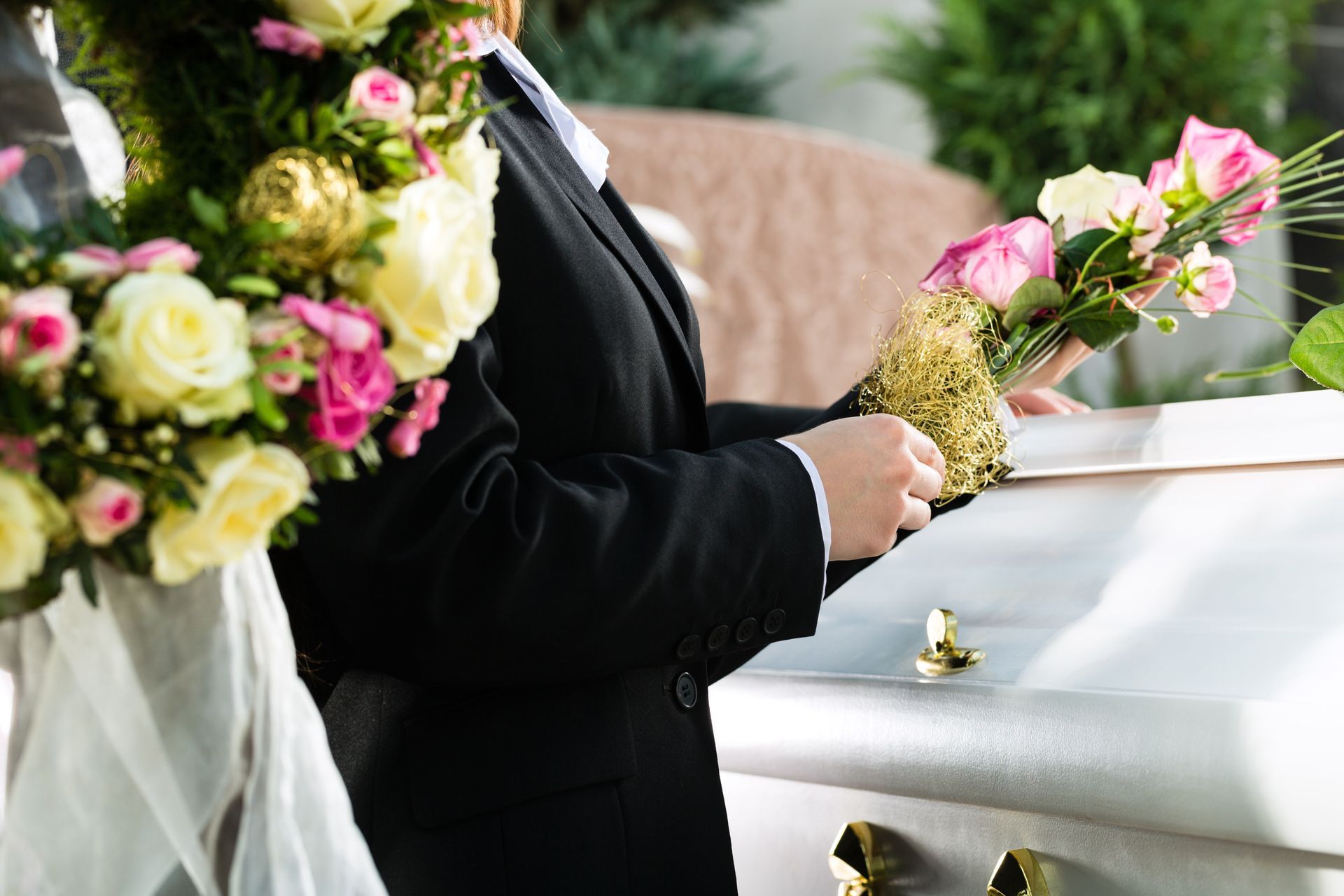 Un hombre con traje sostiene flores delante de un ataúd.