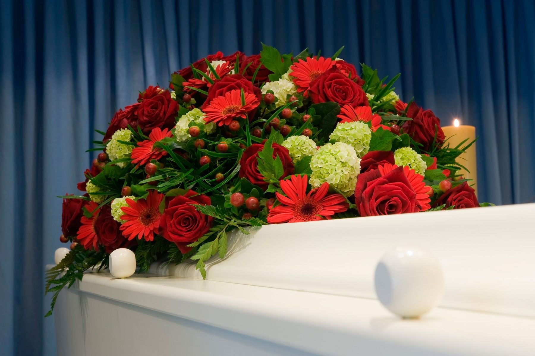 Un ataúd blanco con flores rojas y verdes.