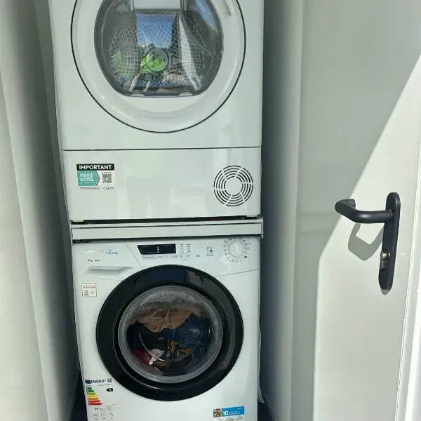 Lavadora y secadora blancas apiladas en un cuarto de lavandería con la puerta entreabierta.