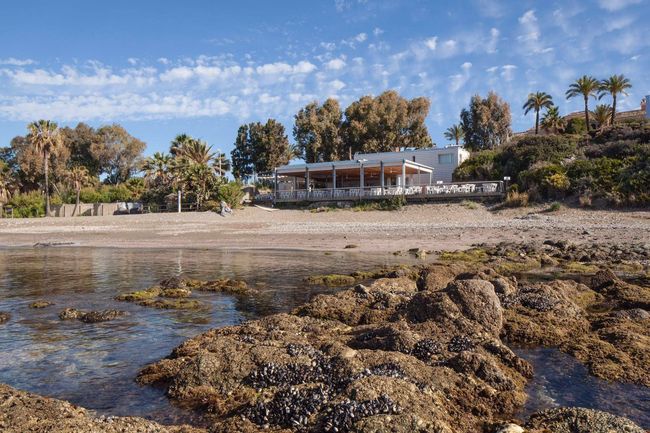 Una playa con rocas y una casa al fondo.