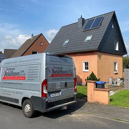Ein Lieferwagen parkt vor einem Haus mit Solarzellen auf dem Dach.