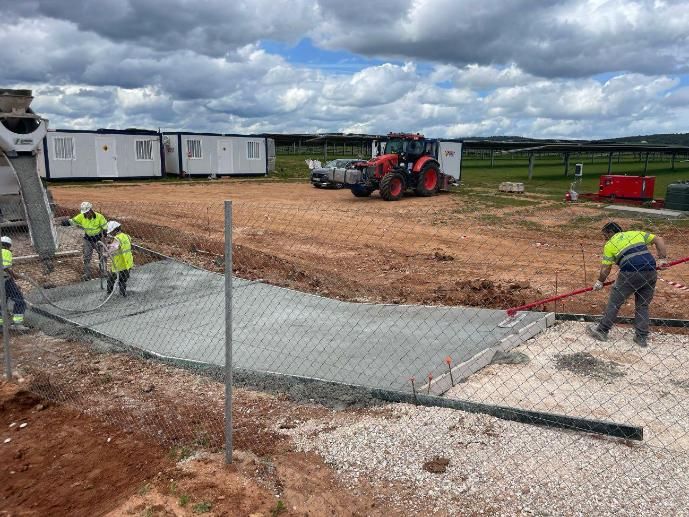 Obreros de la construcción vierten y alisan el hormigón en una obra con un tractor y edificios portátiles.