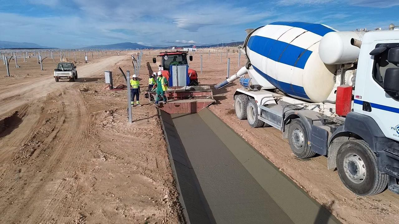 Camión de hormigón vierte hormigón en un molde en un camino de tierra en un sitio de construcción; trabajadores cerca.